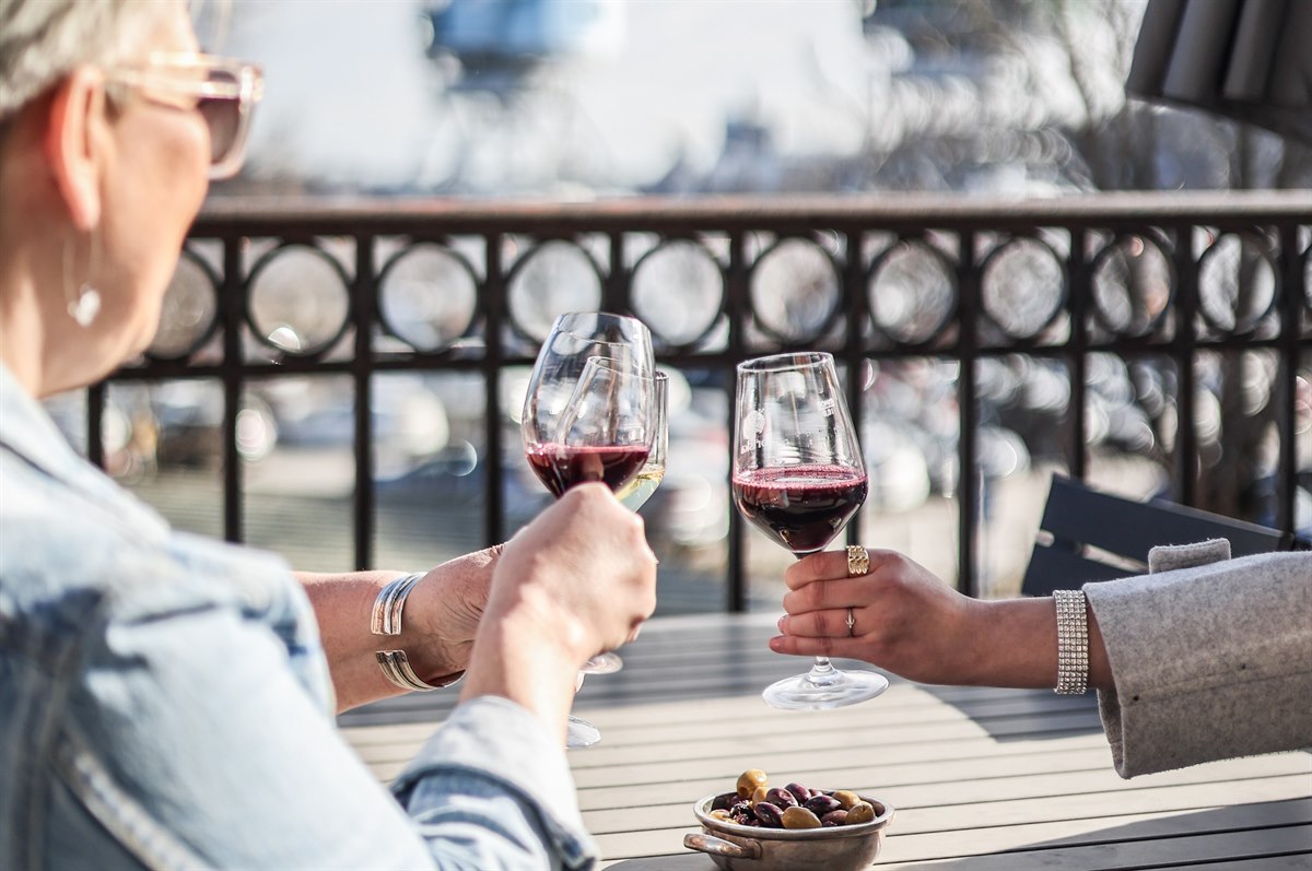 A person on a porch looking a the view and holding a wine glass.