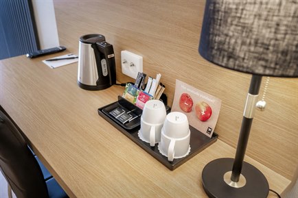 A desk with cups, a kettle, a lamp, pen and papers.