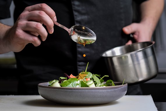 Chef pours sauce over a dish. Photo.
