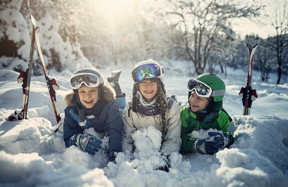 Three kids are lying in the snow. Image.