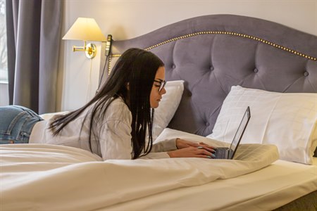 A woman lying in a bed with a pc. Image.