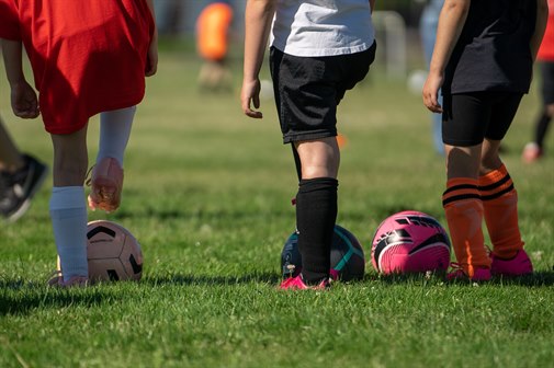 Three children with fotballs photographed from behind.