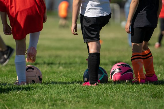 Three children with fotballs photographed from behind.