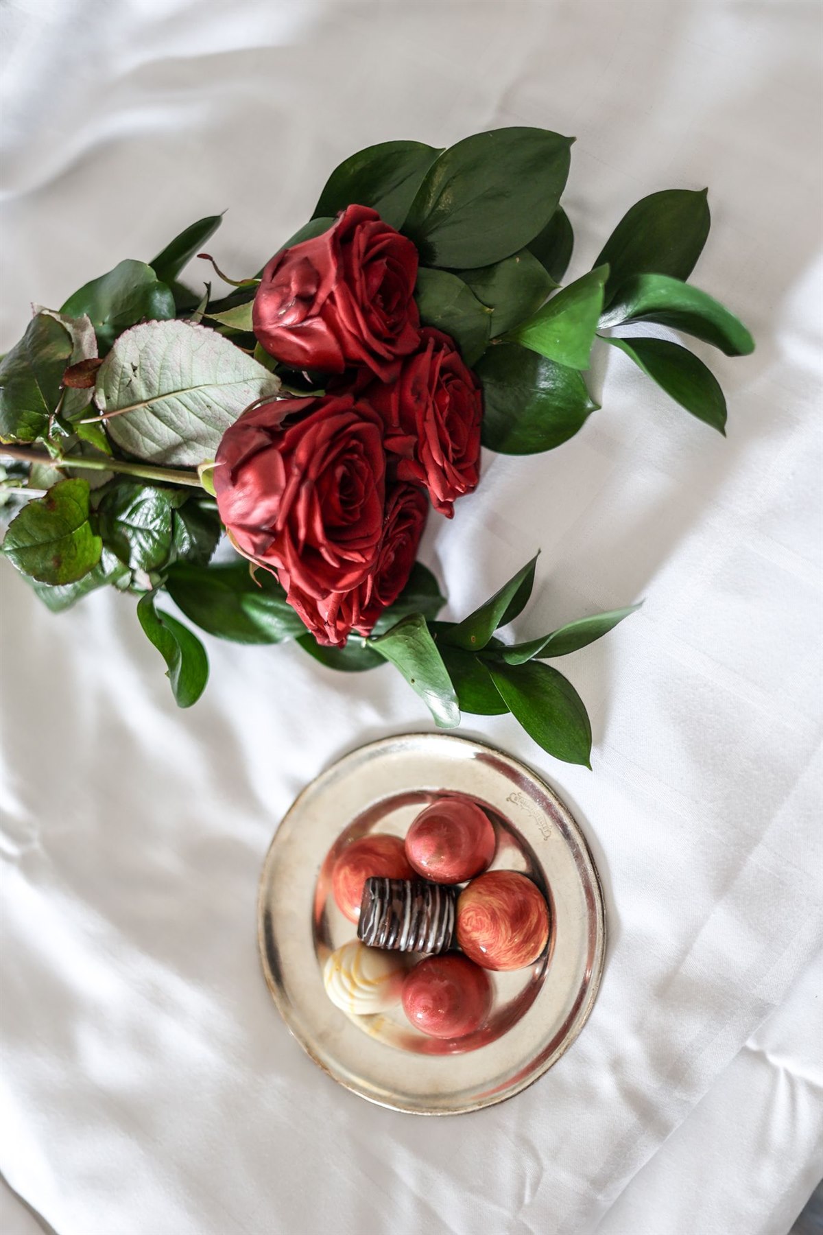 Roses and chocolate pralines on a bed.
