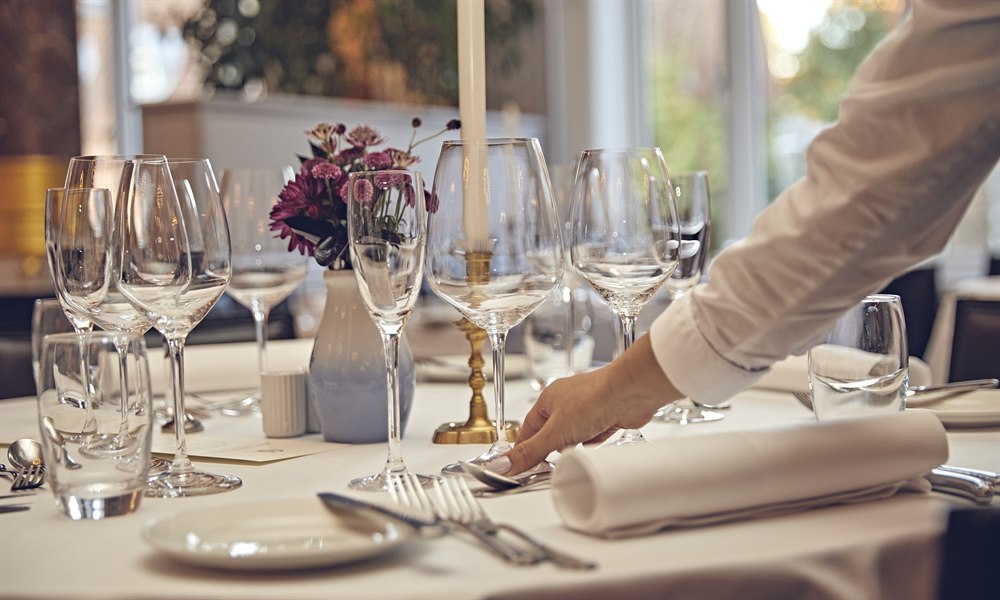 En hånd sætter et glas ned på et dækket restaurantbord. Foto.