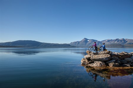 To personer med sykler på en klippe med utsikt over en innsjø.