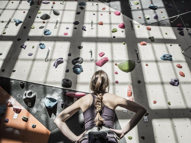 En ung flicka tittar upp på en inomhus klättervägg.