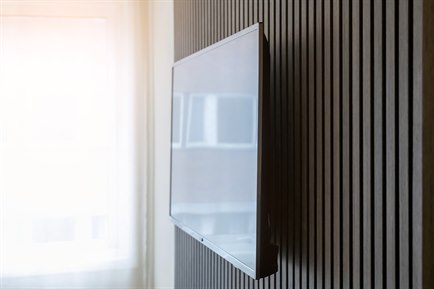 A wall with a TV beside a window with a white transparent curtain.