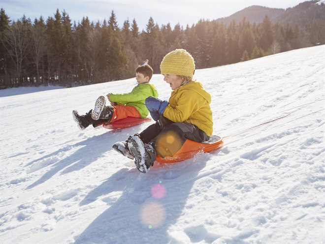 Barn åker pulka i en snöfylld backe.