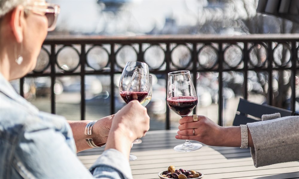 A person on a porch looking a the view and holding a wine glass.