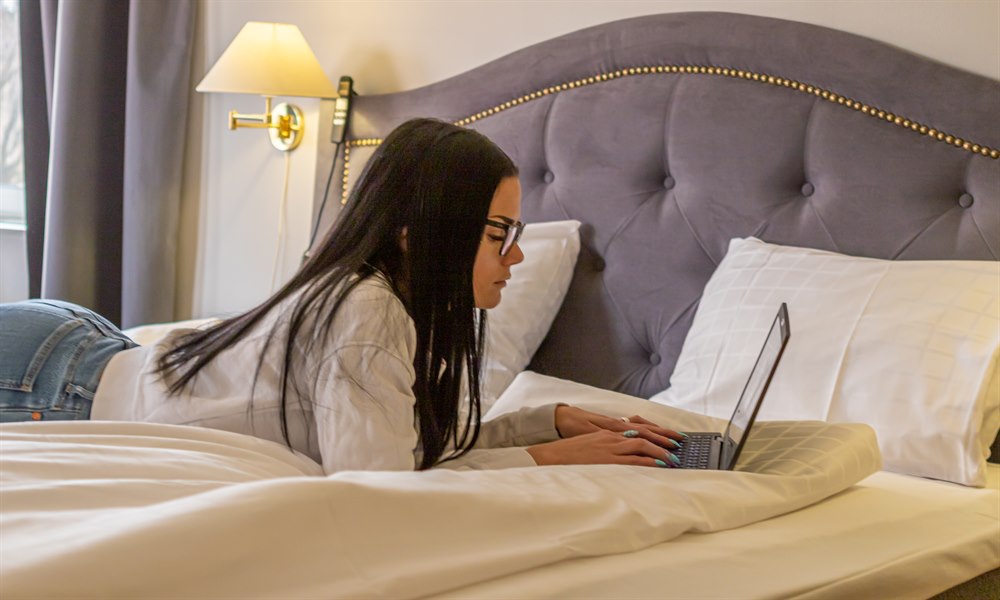 A woman lying in a bed with a pc. Image.