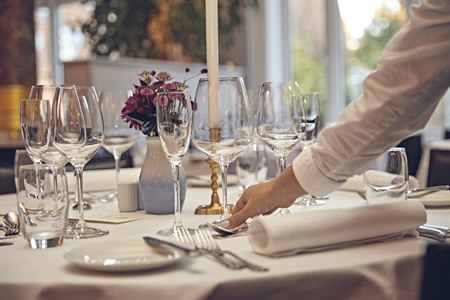 En hand sätter ner ett glas på ett dukat restaurangbord. Foto.