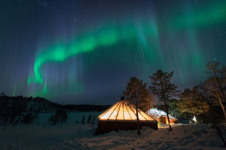 Nordlys danser på himmelen over et opplyst telt.